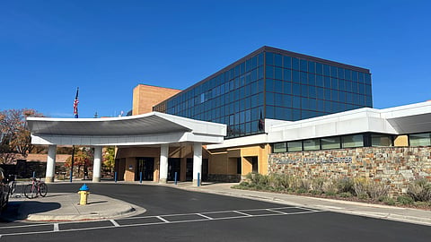 A hospital building with a road in front and a blue building in the back.