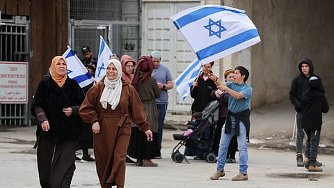 Muslim women walk, as Israeli settlers carry Israeli flags next to a checkpoint near the Ibrahimi mosque, also known as the Cave of Patriarchs, on the day of the first Friday prayers of Ramadan, in Hebron's Old City, in the West Bank 