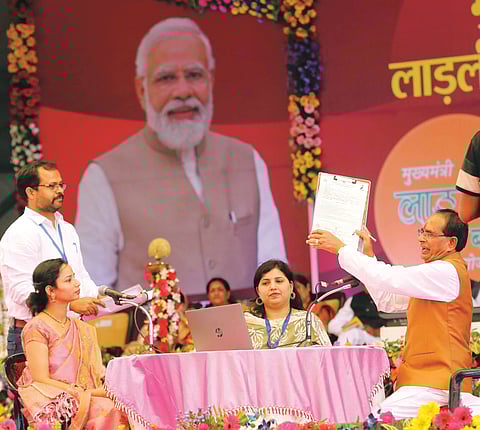 Chief Minister Shivraj Singh Chouhan helps a beneficiary to fill her form for granting Rs 1,000 per month during the launch of Ladli Behna Yojna 
at Jamboree ground in Bhopal on Sunday.