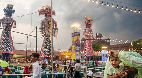 A man covers himself and a child under a plastic sheet amid rainfall during the 'Dussehra' festival celebration organised by Nav Shri Dharmik Lila Committee, at the Red Fort, in New Delhi, Thursday, Oct. 2, 2025.