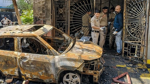 Police personnel gather near the wreckage of a car after a fire broke out in a house, in Indore, Madhya Pradesh, Wednesday, March 18, 2026.