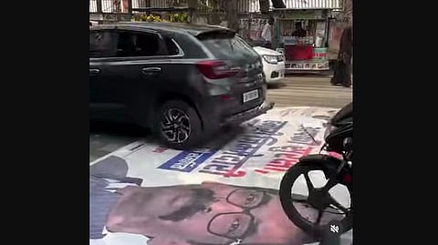 Vehicles drive over a poster of Hemant Soren laid out on the road.