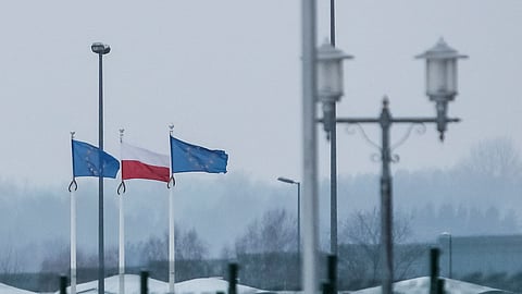 FILE PHOTO: A view from the Belarusian side of the frontier shows Polish and EU flags behind a fence at the Bruzgi-Kuznica checkpoint on the Belarusian-Polish border amid the migrant crisis in the Grodno region, Belarus, December 23, 2021. 