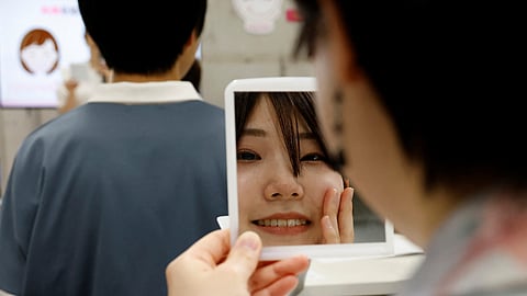 A student practices smiling with a mirror at a smile training course at Sokei Art School in Tokyo, Japan, May 30, 2023. 