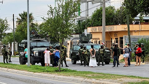 FILE PHOTO: People stand next to Mexican soldiers guarding a crime scene where five men were killed following a chase by federal forces, in Nuevo Laredo, Mexico May 18, 2023. 
