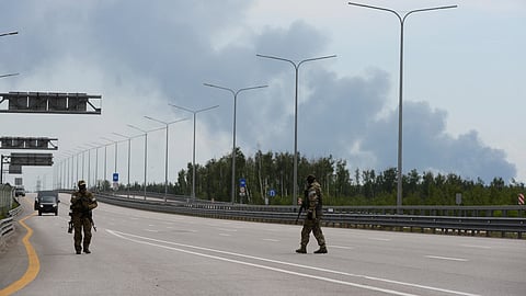 Fighters of Wagner private mercenary group walk during a stop on M-4 highway, which links the capital Moscow with Russia's southern cities, with smoke from a burning fuel tank at an oil depot seen in the background, near Voronezh, Russia, June 24, 2023. 