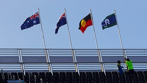 FILE PHOTO: Workers raise the flag of the Torres Strait Islands next to an Australian Aboriginal flag, the Queensland state flag and the Australian national flag on a stand above the Commonwealth Games competition swimming pool on the Gold Coast in Australia, April 3, 2018. 