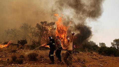 Men help a firefighter as they try to extinguish a wildfire burning near the village Vlyhada, near Athens, Greece, July 19, 2023. 