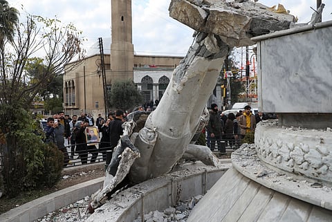 People stand near a damaged statue of former Syrian president Hafez al-Assad after Syrian rebels announced that they have ousted President Bashar al-Assad, in Qamishli, Syria December 8, 2024. 