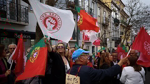 People wave flags of the Socialist party (PS) as a man wears a card reading, "To be socialist is not a sin", while waiting for PS leader Pedro Nunes Santos, for a rally ahead of the snap elections, in Lisbon, Portugal, May 13, 2025. 