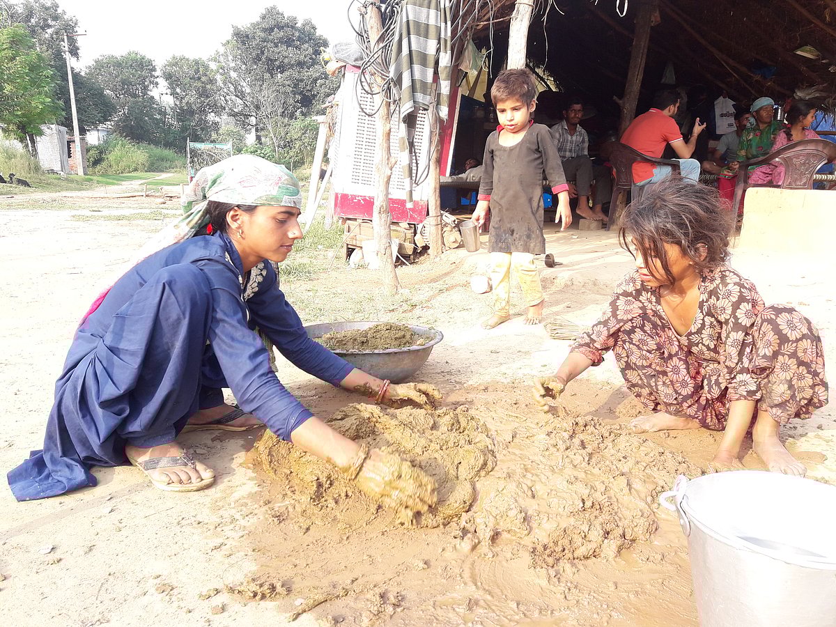 Tribal girls mixing mud and straw to make daub to put on the walls of their huts. 