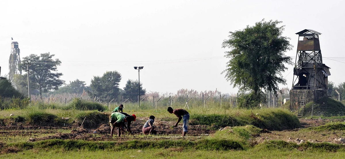 A file picture of villagers farming between Pakistan tower (L) and Indian BSF post along with the fence at International Border in Garkhal village, Pargwal in Jammu sector.
