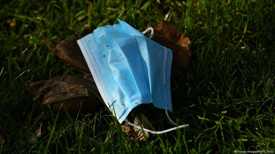 image of a surgical mask left on grassy ground, covering a mound of dirt 