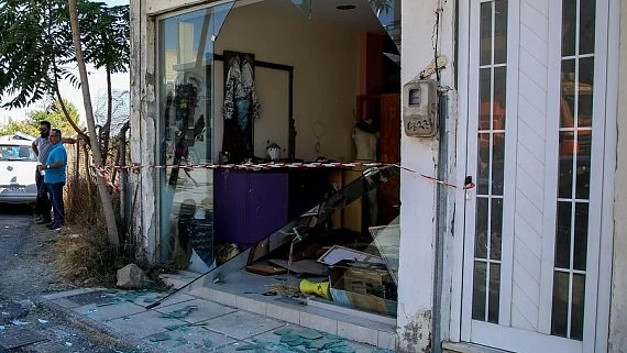 People stand outside a house damaged in an earthquake in Arkalochori