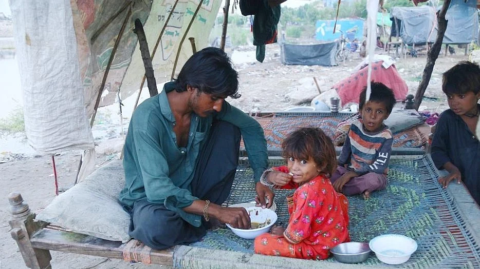 A flood-affected man with children eats food at a makeshift tent in Jamshoro district in Pakistan's Sindh province on Sept. 8, 2022. (Photo: Str/Xinhua/IANS)