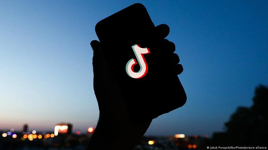 The silhouette of a hand holding up a phone which has the TikTok logo on the screen (DW)
