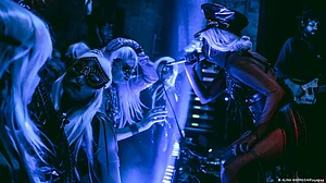 Ganna Nikitina holding a mic, surrounded by masked performers