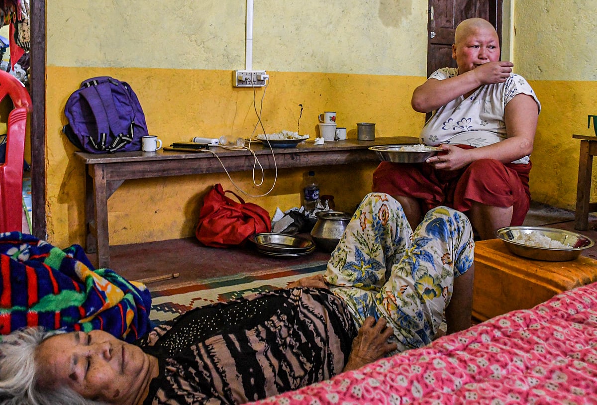 Churachandpur, Manipur: Cancer patient Chinkhothang Baite (47) eats lunch while her sick mother is lying on a bed in a relief camp at Rengkia village (photo: Getty Images)