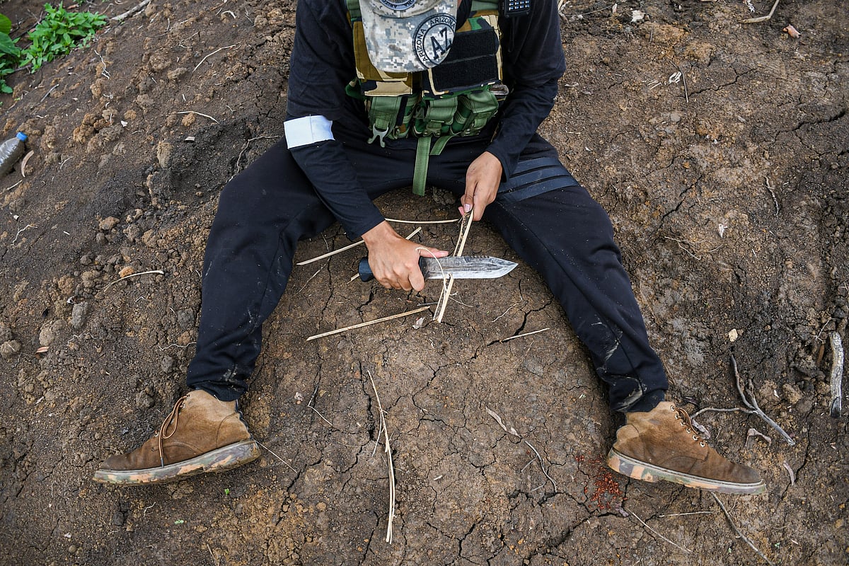 A Kuki youth who volunteered to guard his village shows the sharpness of his knife by peeling bamboo while on duty outside his bunker on the boundary line that divides this area in Churachandpur into two ethnic zones (photo by Biplov Bhuyan/SOPA Images/LightRocket via Getty Images)