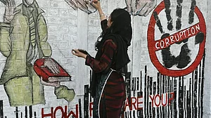 A woman graffitis an anti-corruption mural on a wall (representative image: @anticorruption/X)