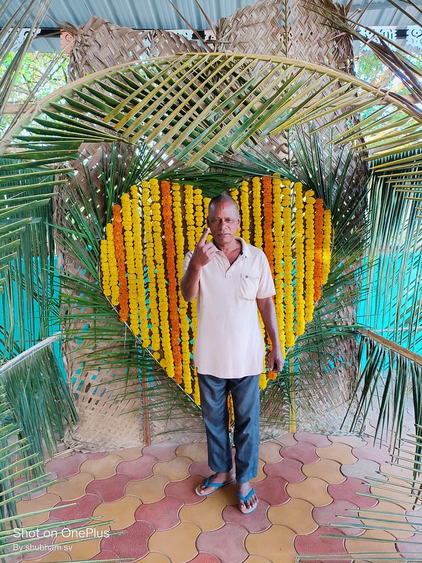 One more senior citizen holds up his inked index finger at selfie spot with palm leaves and a marigold heart (photo courtesy @ECISVEEP/X)