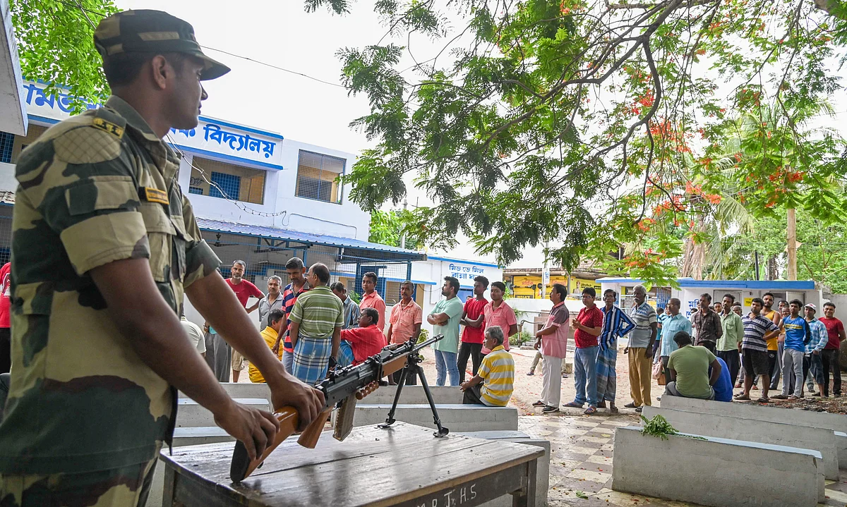 A BSF jawan stands guard as people queues outside a polling booth in Hooghly district, West Bengal (photo: PTI)