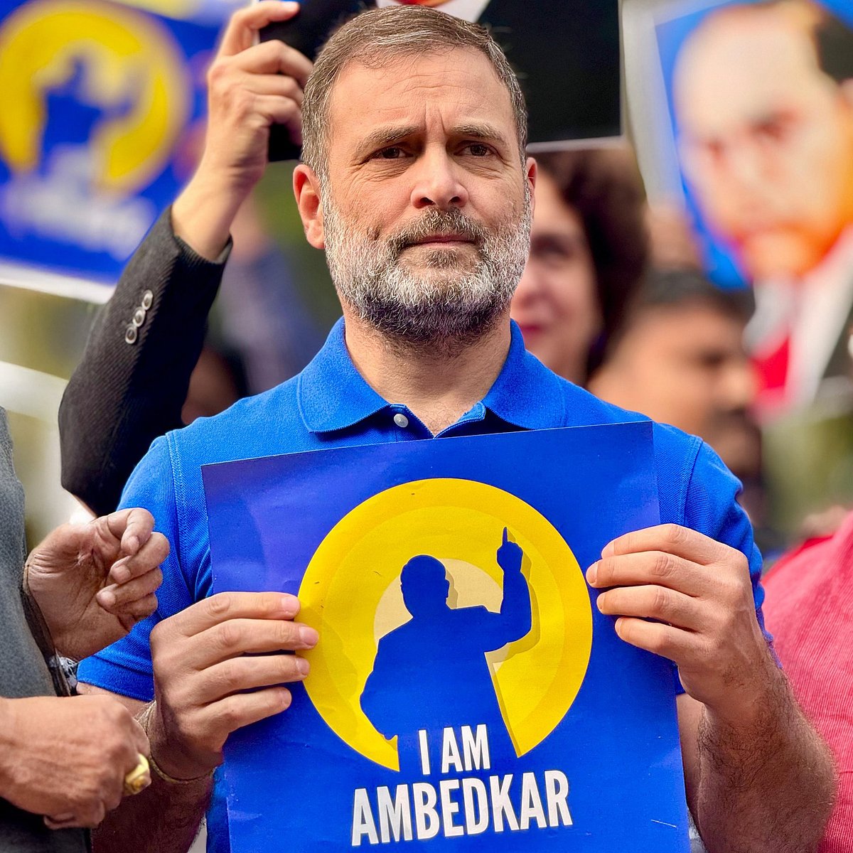Rahul Gandhi, dressed in blue, holds up a poster with a silhouette of B.R. Ambedkar in blue, with the legend 'I am Ambedkar'