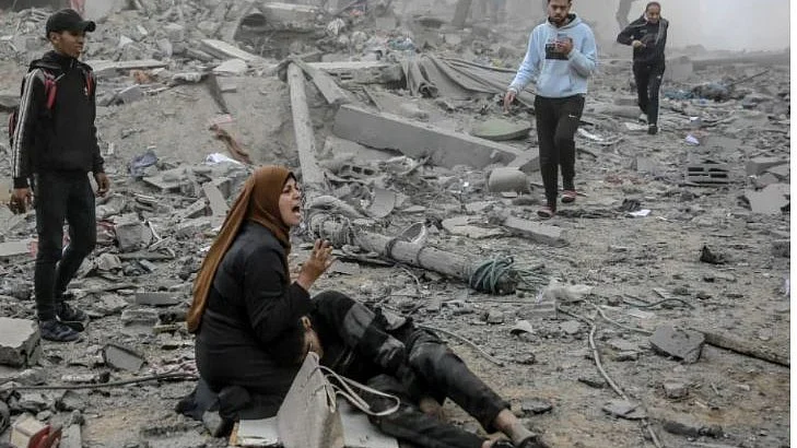 Woman in Gaza holds an injured person (likely a child), calling out as others rush across rubble to help
