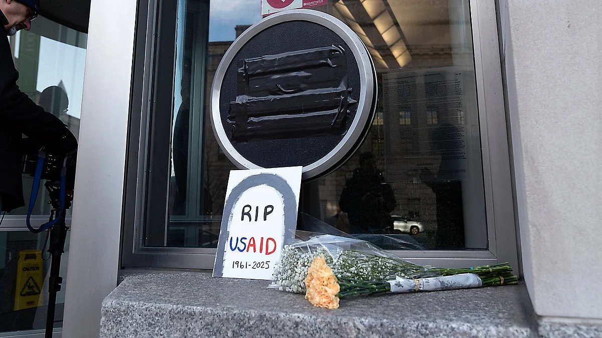 A bouquet and a card featuring a tombstone that reads 'RIP USAID (1961–2025) outside an USAID office