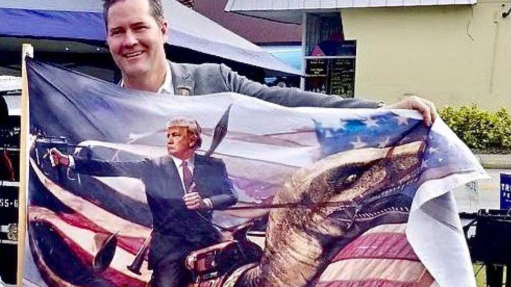 Mike Waltz in 2021, with a flag depicting Donald Trump riding a... dinosaur?!  