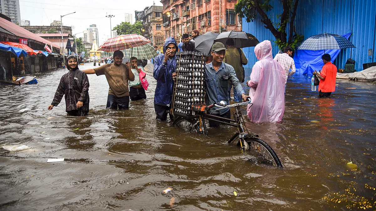 People wade through a flooded road during heavy rain in Mumbai on 26 May (photo: PTI)