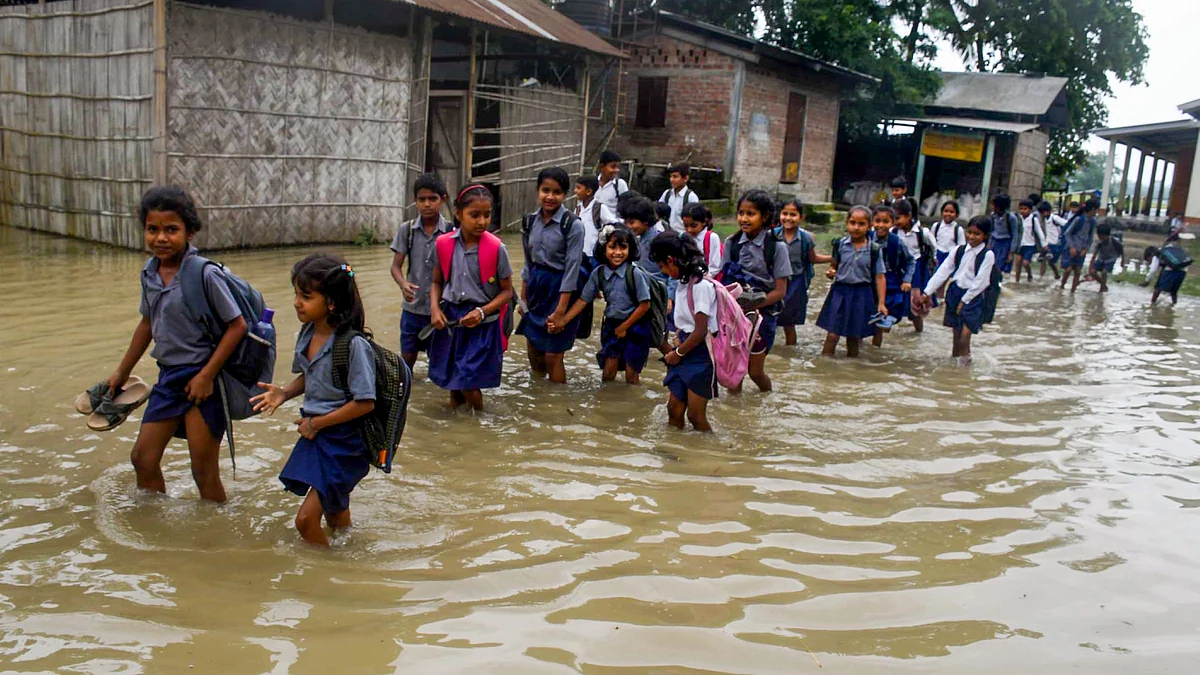 School children wade through a flooded road in Darrang on 3 June (photo: PTI)