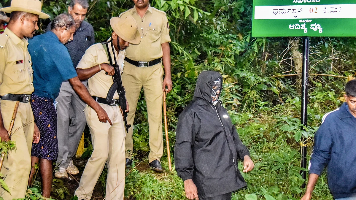 Security personnel with the whistleblower near an alleged burial site in Dharmasthala (photo: PTI)