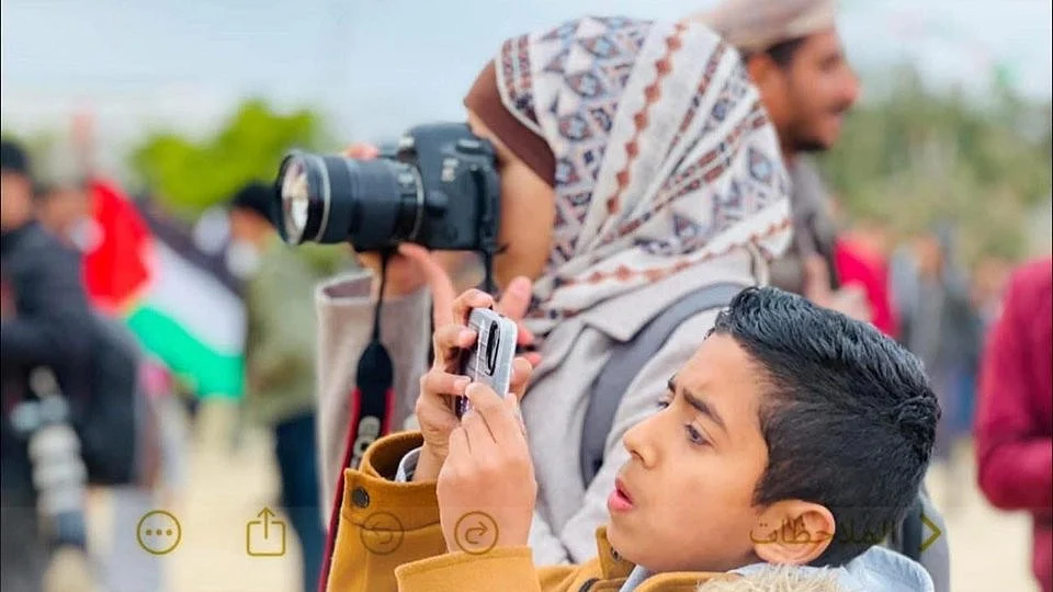 Gaza journalist Mariam Dagga shoots through her camera, her son grabs his own shot on a phone