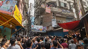 Crowds pack a narrow Old Dhaka lane after a quake collapses a roof and wall.