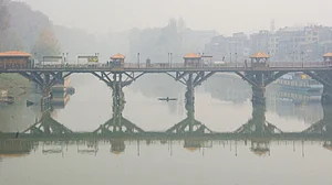 A man rows a boat across the Jhelum river on a hazy day in Srinagar.