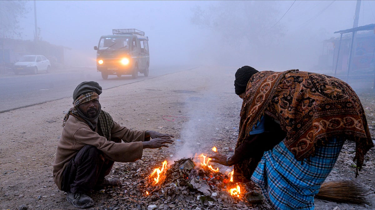 People sit around a bonfire amid dense fog on a cold winter morning, in Ranchi.