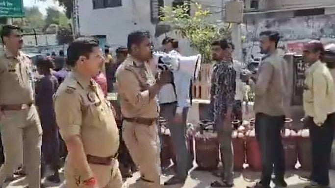 Police personnel walking past a long queue of residents standing with empty LPG cylinders