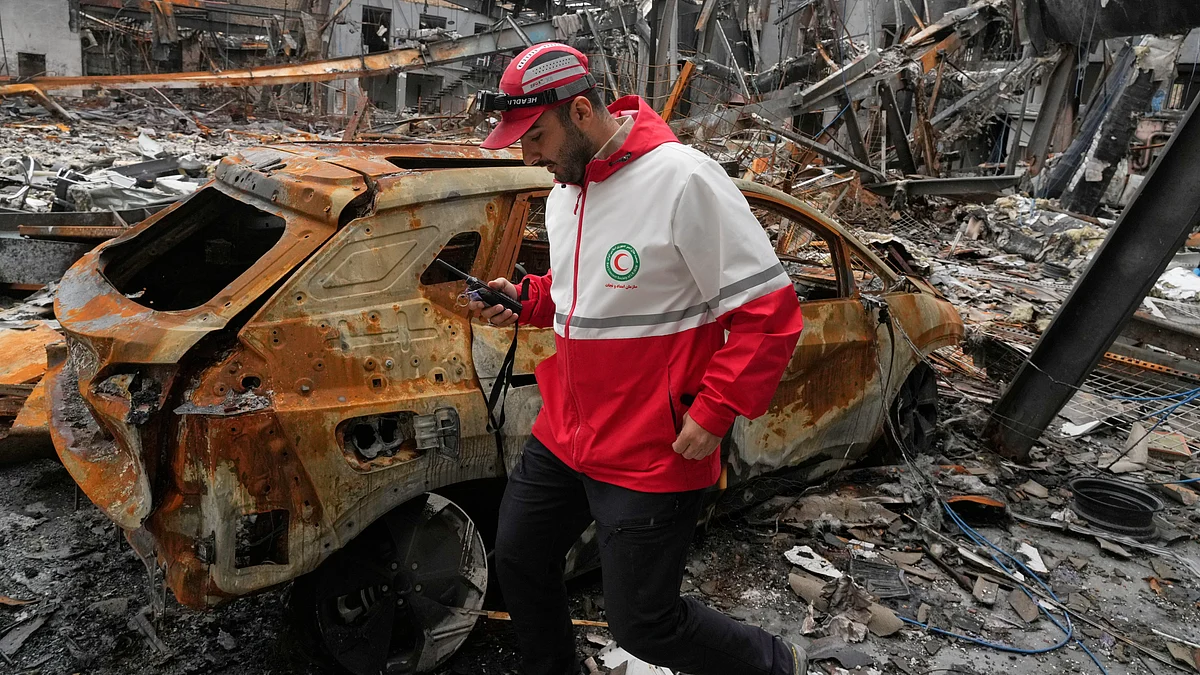 An Iranian Red Crescent member walks past a damaged vehicle following reported strikes.