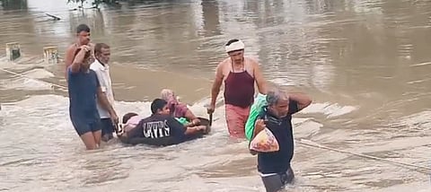Villagers Cross a Flooded Culvert in a Large Iron Pan During Heavy Rain
