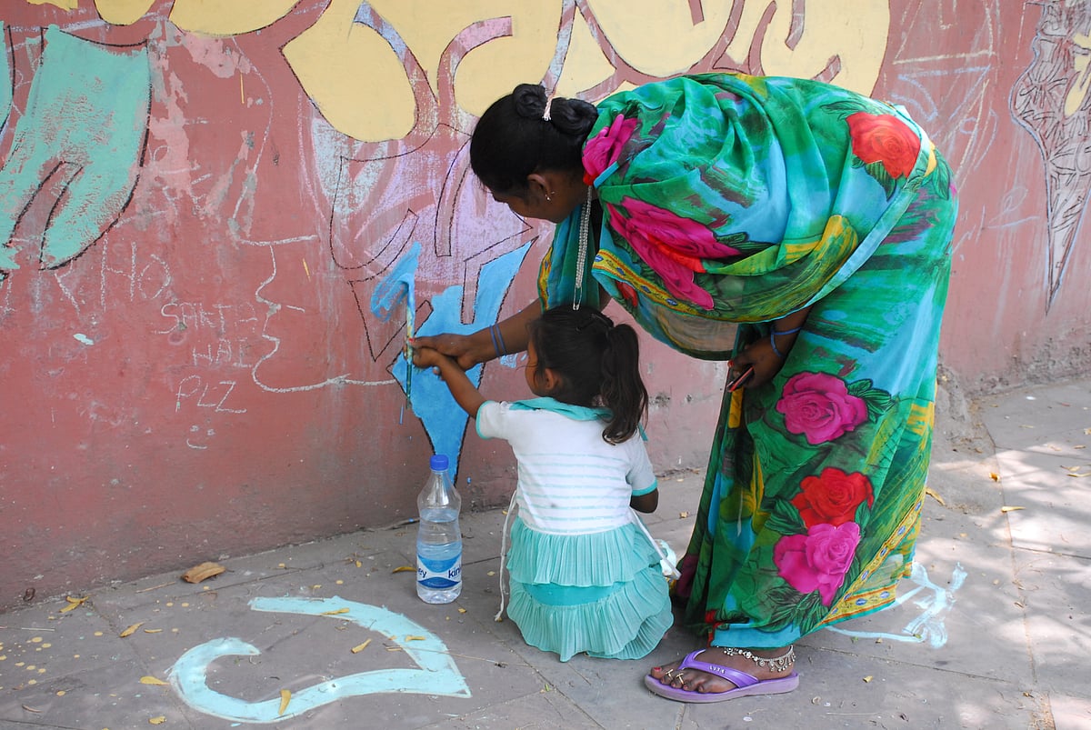 दीवारों पर बच्ची को रंग भरना सिखाती महिला