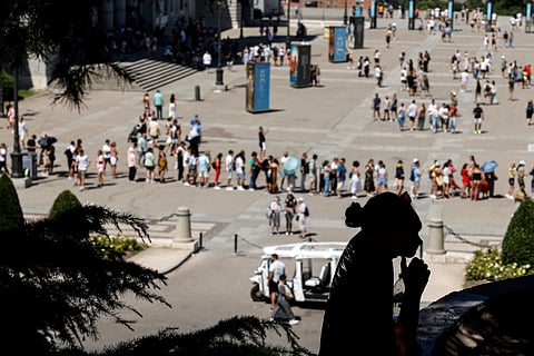 A Tourist rests under the shade of trees in front of tourists queuing at the Palacio Real