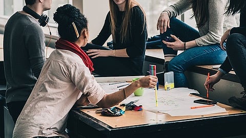 A group of people gathered around a table, collaborating on a project with papers and stationery.