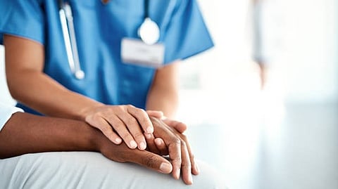 A healthcare worker gently holding a patient’s hand in support.