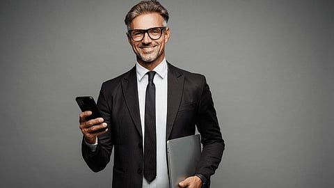 Smiling businessman in a suit holding a laptop and smartphone