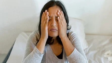 Woman sitting with her hands on her face, appearing tired or stressed.