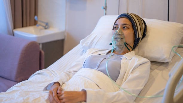 A woman lying in a hospital bed wearing an oxygen mask.