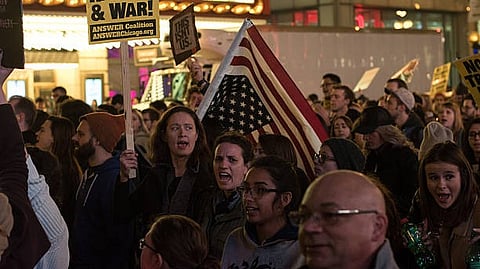 People protesting with signs and an American flag in a crowded street.