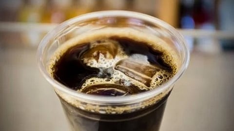 The image shows a close-up of a glass filled with iced black coffee and foam on top.