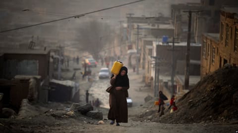A woman carries water in a plastic container as she ascends a slope on the way toward her home in Kabul. [RFE/RL]